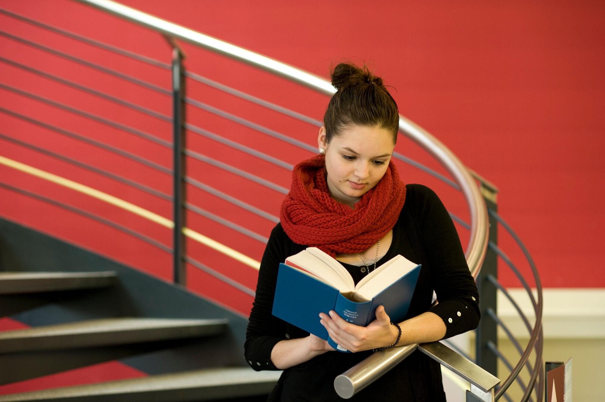 Studentin mit Buch in der Hand auf einer Treppe in der Bibliothek
